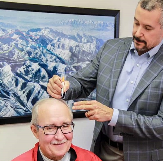A man in a blazer examines another man's scalp.