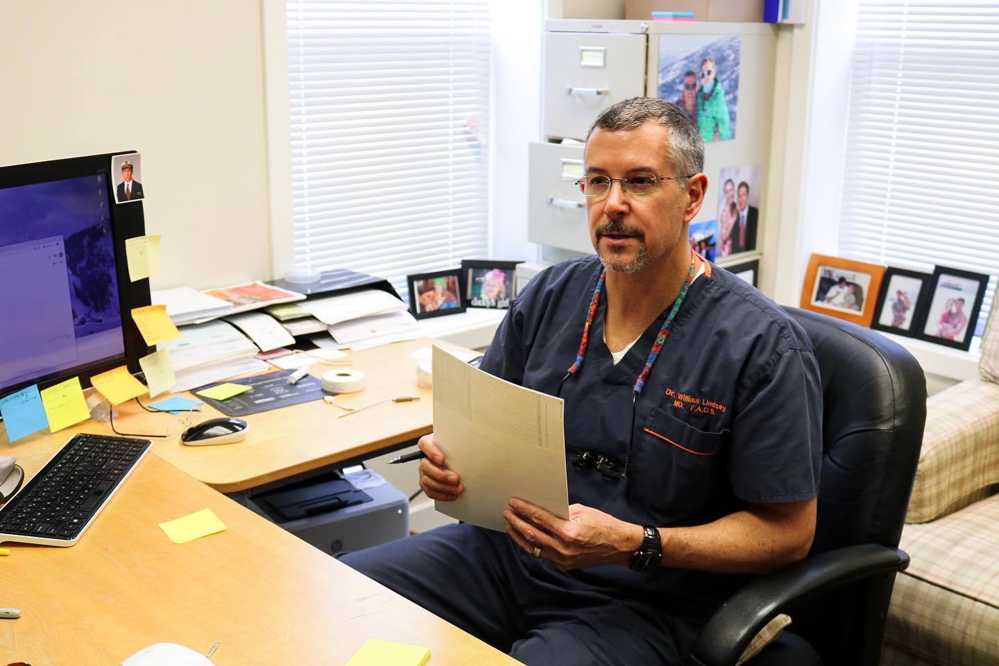 Doctor in blue scrubs holding a document in his office.